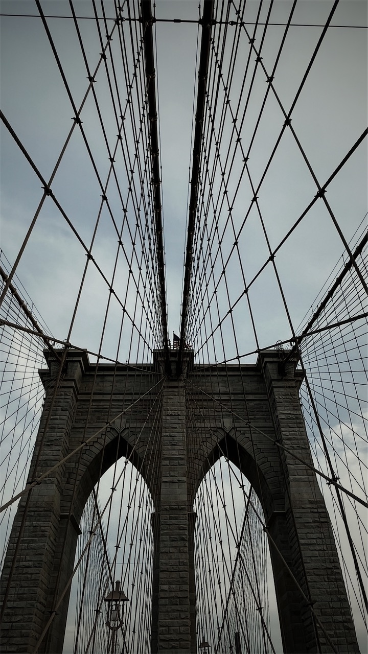 Looking up at a stone tower of the Brooklyn Bridge through its cables